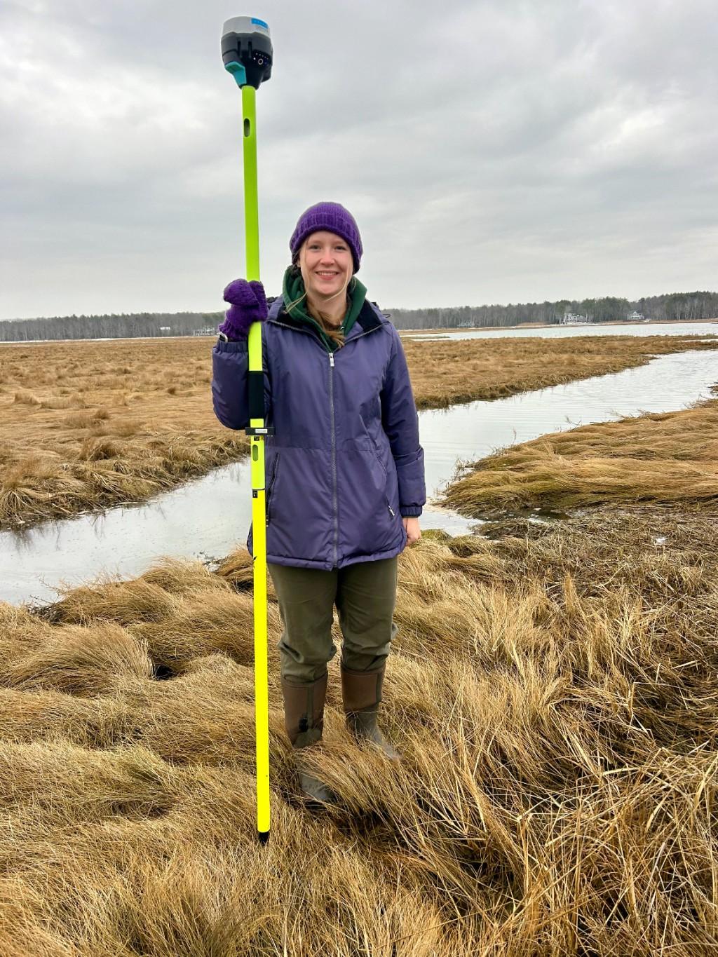 Katelyn DeWater holds land survey equipment in the Biddeford Pool salt marshes